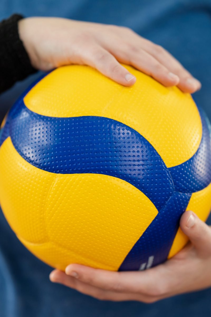 Bright new volleyball ball in hands of a young girl player. Beautiful photo of a new professional ball in female hands on court