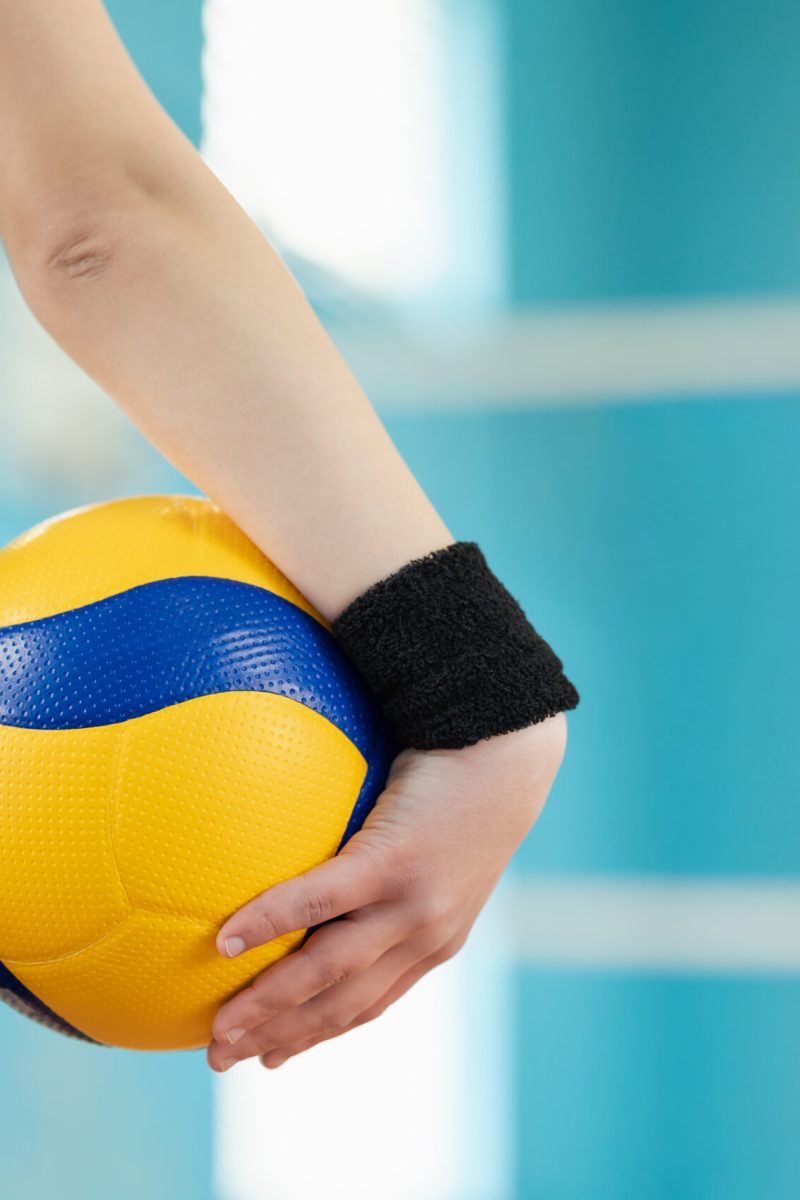 Back view of volleyball ball in hand of a female player standing in gym, close up. Training, volleyball game, mastering skills concept